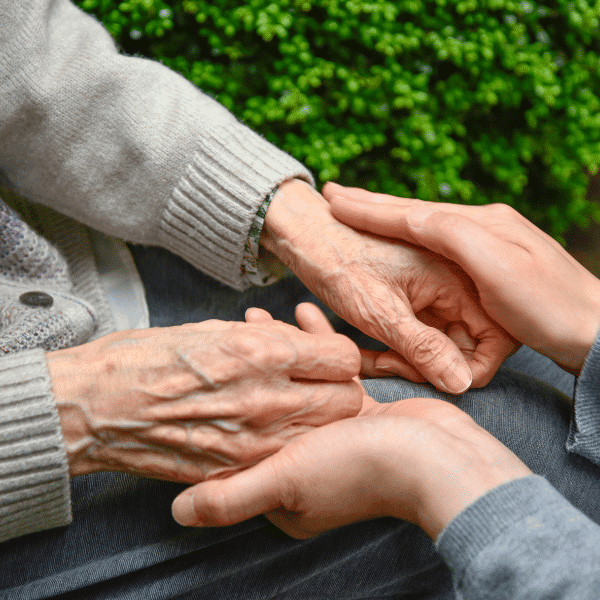 A young dedicated dementia specialist holds the hands of am elderly resident.